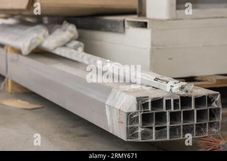 Viele oder mehrere miteinander verbundene Aluminiumprofile, die zum Laserschneiden bestimmt sind. Charge oder Packung mit quadratischen Aluminiumschläuchen auf dem Boden. Stockfoto