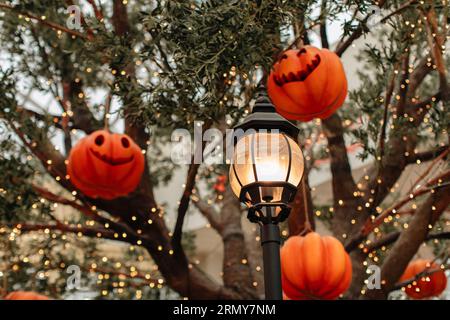 Heller Kürbis mit einem gruseligen Halloween-Gesicht, das an einem Baum mit Girlanden hängt. Hintergrund für halloween-Party Stockfoto