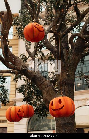 Leuchtend oranger Kürbis mit einem gruseligen Halloween-Gesicht, das an einem Baum mit Girlanden hängt. Vertikaler Hintergrund für halloween-Party Stockfoto