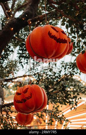 Leuchtend oranger Kürbis mit einem gruseligen Halloween-Gesicht, das an einem Baum mit Girlanden hängt. Hintergrund für halloween-Party Stockfoto