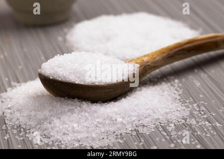 Nahaufnahme von grobem weißem Meersalz in einem Stapel auf dem Tisch und auf dem Löffel in einem Studio-Setting. Stockfoto