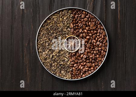 Grüner trockener Tee, Kaffeebohnen und eine Scheibe trockener Zitrone in einer runden Box auf einem dunklen hölzernen Hintergrund von oben. Stockfoto