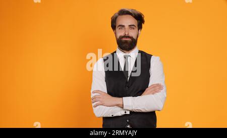 Der Kellner im Restaurant posiert im Studio und fühlt sich selbstbewusst, während er sich darauf vorbereitet, die Leute zu bedienen. Mann, der in der Feinschmeckergastronomie arbeitet und formellen Anzug als professioneller Luxus-Butler trägt. Stockfoto