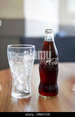 Flasche Coca Cola auf einem Tisch mit einem Glas voll Eiswürfel Stockfoto