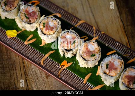 Blick von oben auf verschiedene Sushi-Brötchen mit Fisch und Reis mit farbenfroher Creme, serviert auf einem Holztablett über dem Tisch drinnen Stockfoto