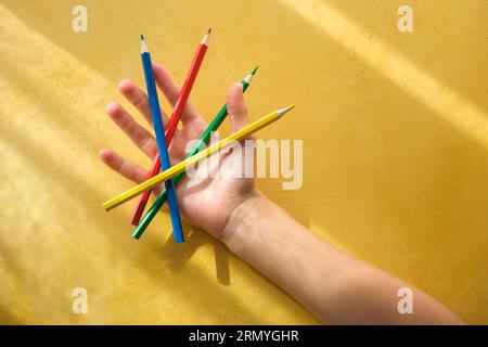 Die Hand eines Kindes pickinDie Hand eines Kindes nimmt Buntstifte auf einem gelben Hintergrund auf. Hochwertige Fotos Stockfoto