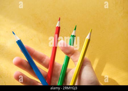 Die Hand eines Kindes pickinDie Hand eines Kindes nimmt Buntstifte auf einem gelben Hintergrund auf. Hochwertige Fotos Stockfoto