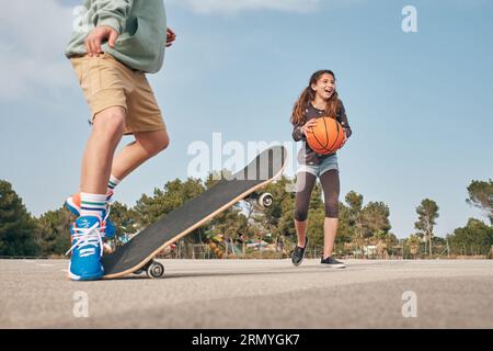 Teenager Junge in Shorts Durchführung Tricks auf Skateboard in der Nähe glückliches Mädchen mit Basketball in der Stadt Sportplatz trainieren Stockfoto