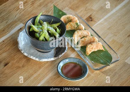 Von oben aus werden köstliche chinesische Töpfchen auf einem Glastablett mit Bananenblättern serviert und auf den Tisch neben einer Schüssel grüner Sojabohnen mit Salz gestellt Stockfoto