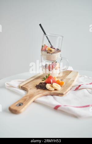 Köstliches appetitliches Dessert mit geriebener Schokolade, serviert in Gläsern mit Löffel und Bananenstreifen und Orangenscheiben, die in der Nähe einer Serviette auf Holz liegen Stockfoto