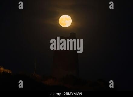 Der blaue Supermond, der zweite Supermond im August, erhebt sich über einem Steinturm (bekannt als „Las Palomas“-Turm) am Strand „La Araña“. Der blaue Supermond ist eines der auffälligsten astronomischen Ereignisse des Monats. Wenn der Vollmond stattfindet, erscheint er größer und heller als normal. Stockfoto