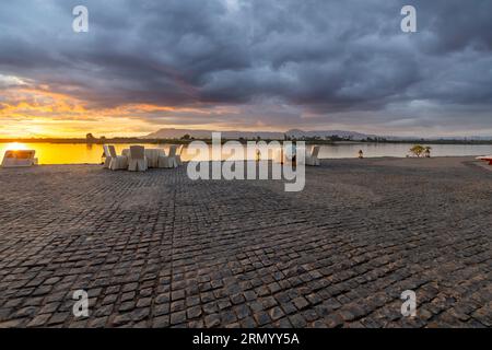 Blick von einem Resort am Flussufer mit Tischen, die das Wasser am Nil unter dem bunten Himmel in der Dämmerung in Luxor, Ägypten, überblicken. Stockfoto