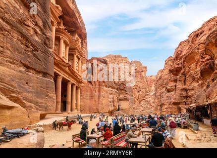 Blick auf das Treasury-Gebäude mit Blick auf den Eingang der Schlucht Siq, mit Kamelen, Pferden und Touristen. Stockfoto