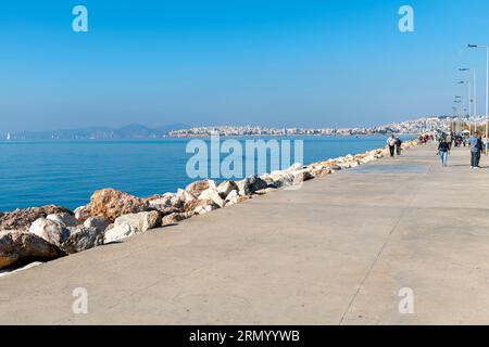 Die Fußgängerzone und Promenade am Meer entlang der Athenischen Riviera in der griechischen Stadt Palaio Faliro, mit Piräus Griechenland im Blick hinter. Stockfoto