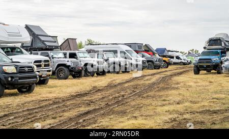 Loveland, CO, USA - 26. August 2023: Wohnmobile, SUVs mit Brutzelten und Jeeps parken in einer Reihe auf einem belebten, matschigen Campingplatz. Stockfoto