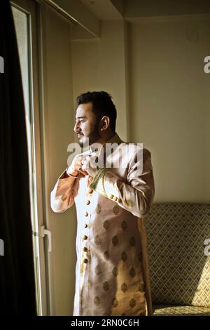 Der nepalesische Bräutigam, der mit einem zarten rosa Sherwani-Mantel verziert ist, steht am glücklichen Tag seiner Hochzeit bereit und strahlt Vorfreude aus. Stockfoto