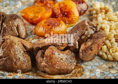 Hühnerleber mit getrockneten Aprikosen und Hirsenbrei auf Platte auf Holzbrett. Nahaufnahme. Stockfoto