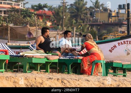 Calangute, Goa, Indien - Januar 2023: Zwei indische Touristen, die eine Massage von einer Frau in einer Strandhütte erhalten. Stockfoto