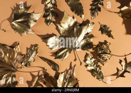 Metallisch-goldene Herbstblätter auf orangefarbenem Hintergrund Stockfoto