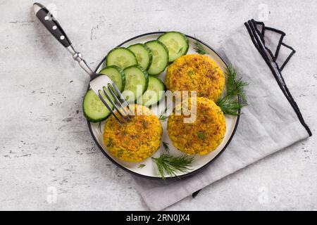 Köstliche Hirseschnitzel mit Karotten und Samen, serviert mit Gurke und Kräutern auf grauem strukturiertem Hintergrund, Draufsicht. Hausgemachtes veganes Essen. Stockfoto