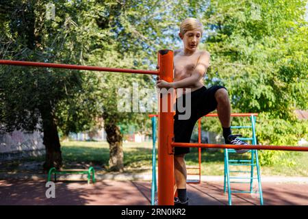 Der Junge im Schulpark kletterte auf die Spitze der horizontalen Bar. Street Workout auf einer horizontalen Bar im Schulpark. Stockfoto