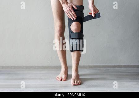 Männliche Beintragende Kniestrecke auf grauem Hintergrund. Orthopädisch-Anatomische Orthesen. Zahnspangen zur Kniegelenkfixierung, Verletzungen und Schmerzen. Fussorthesen-Tutor Stockfoto