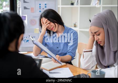 Zwei frustrierte und enttäuschte asiatische Geschäftsfrauen oder weibliche Büroangestellte fühlen sich traurig und gestresst über ihr erfolgloses Projekt. Stockfoto