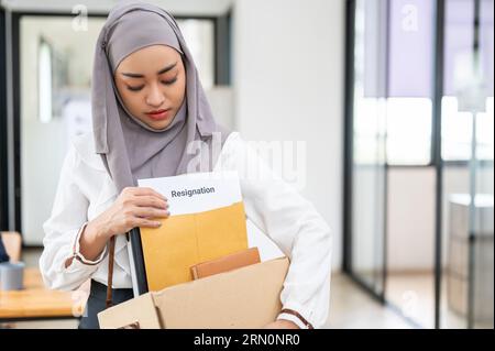 Traurige und verärgerte junge asiatische muslimische Büroangestellte verlässt das Büro mit einer Pappschachtel und ihrem Rücktrittsbrief. Zurücktreten, Job verlassen, Stockfoto