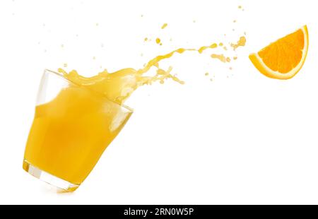 Geneigtes Trinkglas mit auslaufendem Orangensaft und fliegendem Orangenstück isoliert auf weißem Hintergrund. Echtes Studiofoto. Stockfoto