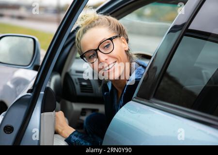 Eine schöne Frau in einer Brille schaut zurück über ihre Schulter, als sie aus einem geparkten Auto aussteigt, in dem sie gefahren ist Stockfoto