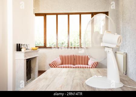 Moderner weißer Elektroventilator im Zimmer auf Holztisch. Stockfoto