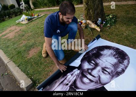 (141205) -- JOHANNESBURG, 5. Dezember 2014 -- Ein Mann entfaltet am 5. Dezember 2014 Ein Poster von Nelson Mandela vor seiner Residenz in Johannesburg, Südafrika. Die Menschen gingen in die Residenz des verstorbenen südafrikanischen Präsidenten Nelson Mandela in Houghton, wo er am 5. Dezember 2013 in Johannesburg, Südafrika, verstarb, um ihr Beileid zum Ausdruck zu bringen und an den 1. Jahrestag des Todes Nelson Mandelas zu gedenken. SÜDAFRIKA-JOHANNESBURG-MANDELA-JAHRESTAG-TOD-GEDENKEN ZhaixJianlan PUBLICATIONxNOTxINxCHN Johannesburg DEC 5 2014 ein Mann entfaltet ein Poster von Nelson Mandela außerhalb seines Wohnsitzes Stockfoto