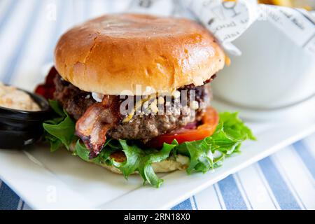 Appetitlicher Burger mit Gemüse, Pommes frites und Sauce auf dem Teller, serviert auf dem Kaffeetisch Stockfoto