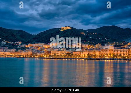 Blick auf die Küste der Stadt Salerno über das Wasser des Mittelmeers, beleuchtet bei Nacht. Stockfoto