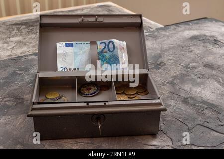 Graue Metall-Kassenschachtel mit 20-Euro-Banknote und Münzen in einem Tablett Stockfoto