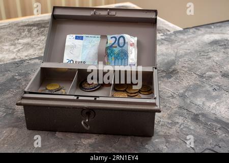 Graue Metall-Kassenschachtel mit 20-Euro-Banknote und Münzen in einem Tablett Stockfoto