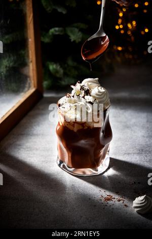 Ein Glas heiße Schokolade mit getupfter Sahne und geschmolzener Schokolade mit einem Löffel. Gemütliches Winterstillleben. Stockfoto