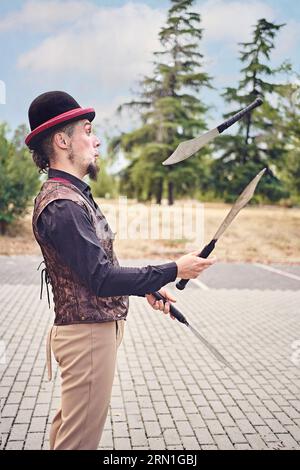 Lustige männliche Performer jonglieren Messer während der Show im Park Stockfoto