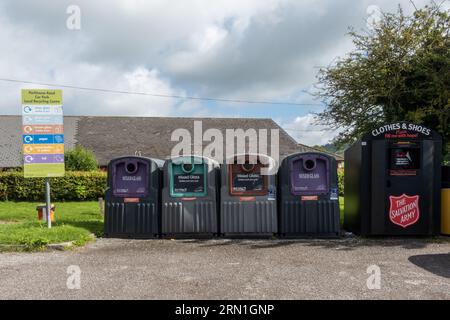 Lokale Recyclingstelle in einem Dorfparkplatz mit Abfalleimern für verschiedene Glasfarben und einem Abfalleimer der Heilsarmee für Textilschuhe, England, Großbritannien Stockfoto