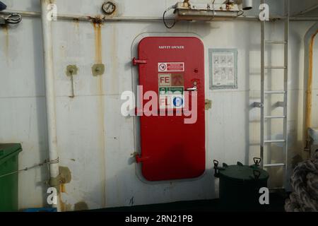 Die rote Metalltür mit Aufklebern schließt den Eingang zum Sicherheitsschloss am Containerschiff. Stockfoto