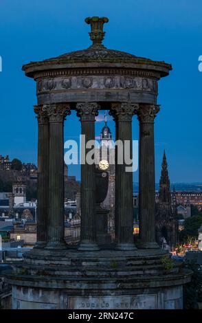 Der Balmoral-Uhrenturm wird durch das Dugald Stewart Monument in Blue Hour, Calton Hill, Edinburgh, Schottland, Großbritannien gesehen Stockfoto