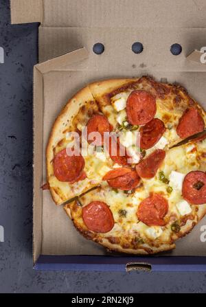 Pizza mit Feta, Chili, Käse und Peperoni - in Pizzapackverpackung Stockfoto