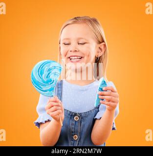 Lutscher, Süßigkeiten und ein Kind lachen im Studio für Süßes, Farbspirale oder Zucker für Energie. Gesicht des glücklichen Mädchens auf orangefarbenem Hintergrund für Stockfoto