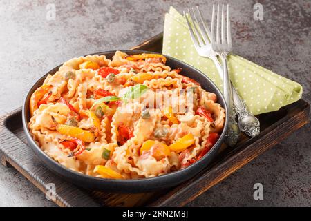 Reginette Pasta mit Paprika und Basilikum in cremiger Tomatensauce mit Kapern auf dem Teller auf dem Tisch. Horizontal Stockfoto