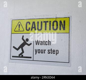Gelbes und schwarzes Warnschild auf Treppen mit der Aufschrift „Pass auf deinen Schritt auf“, das auf eine mögliche Stolpergefahr hinweist, steile Treppen und Vorsicht beim Aufsteigen Stockfoto