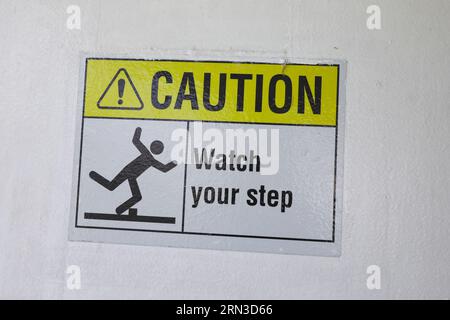Gelbes und schwarzes Warnschild auf Treppen mit der Aufschrift „Pass auf deinen Schritt auf“, das auf eine mögliche Stolpergefahr hinweist, steile Treppen und Vorsicht beim Aufsteigen Stockfoto