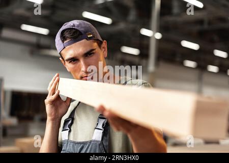 Junger Zimmermann sucht und wählt Holzbohle in einer Werkstatt in einer Holzfabrik Stockfoto