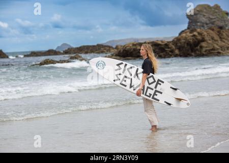 Trevaunance Cove, St Agnes, Cornwall, UK, 21/07/2023 Surfer Against Sewage Tabitha McCormick Surfboard mit dem Slogan "SICK OF SEWAGE" . Stockfoto