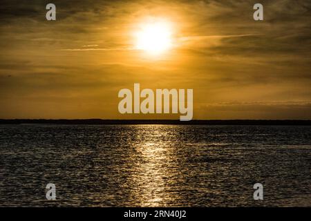 BULLYARD SOUND, South Carolina, USA – Ein lebhafter Sonnenuntergang erleuchtet den Himmel über dem Bullyard Sound in der Lowcountry Region von South Carolina. Das goldene Licht der untergehenden Sonne reflektiert das ruhige Wasser des Gezeitenflusses und erzeugt ein atemberaubendes Farbenspiel über Himmel und Wasser. Silhouetten der Küstenvegetation, wahrscheinlich Spartina-Gras, bilden die Kulisse und zeigen die einzigartige Schönheit dieses Küsten-Ökosystems. Stockfoto