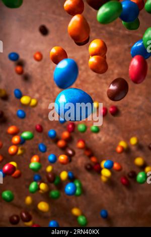 Bild voller fallender Bonbons in verschiedenen Farben auf dunkelbraunem Hintergrund von oben. Stockfoto